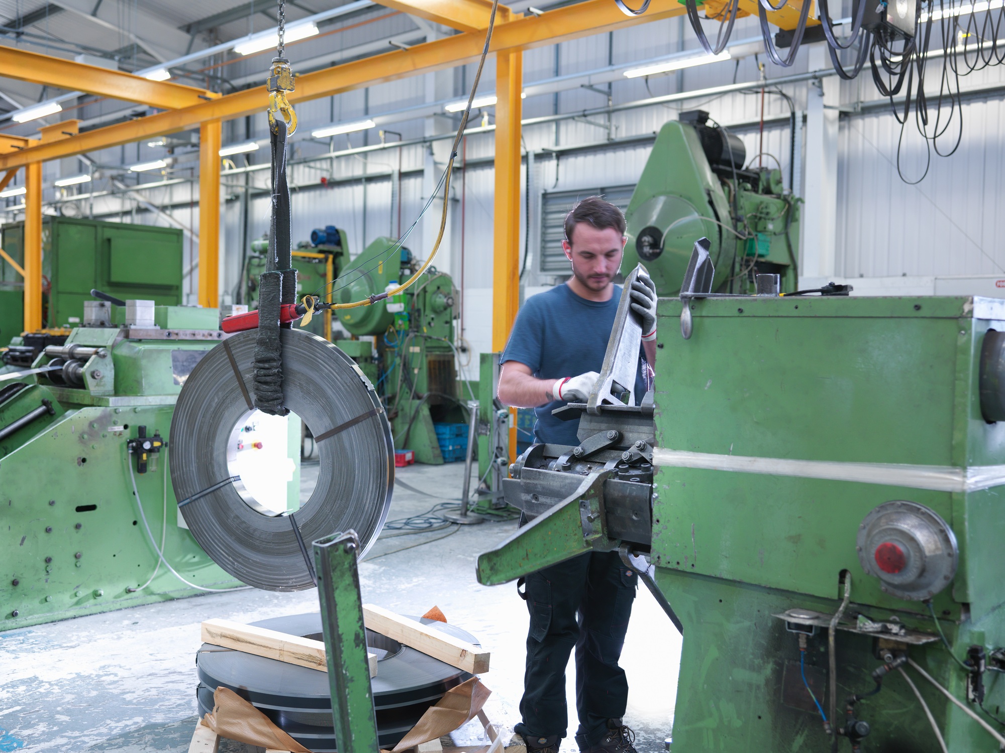 Worker loading rolls of metal into stamping machine in engineering factory